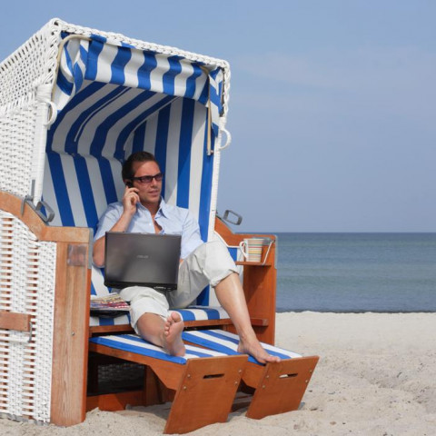Mann sitzt mit Laptop und einer Tasse Kaffee im Strandkorb des Strandhotel Fischlands