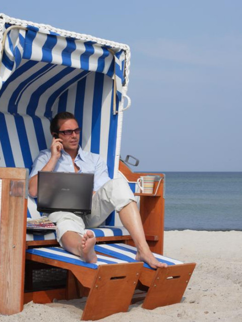 Mann sitzt mit Laptop und einer Tasse Kaffee im Strandkorb des Strandhotel Fischlands