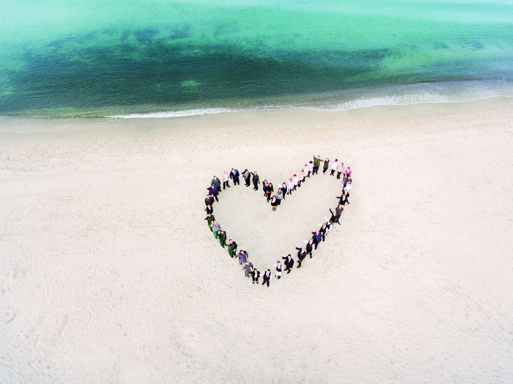 Mitarbeiter des Strandhotelfischlands formen ein Herz am Strand