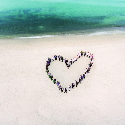 Mitarbeiter des Strandhotelfischlands formen ein Herz am Strand