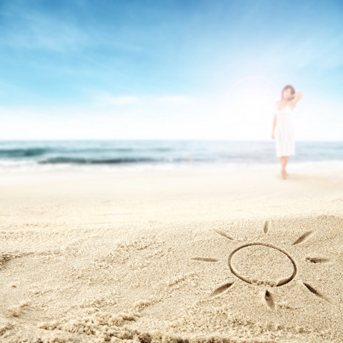 in den Sand gemalte Sonne mit Frau und Ostsee im Hintergrund