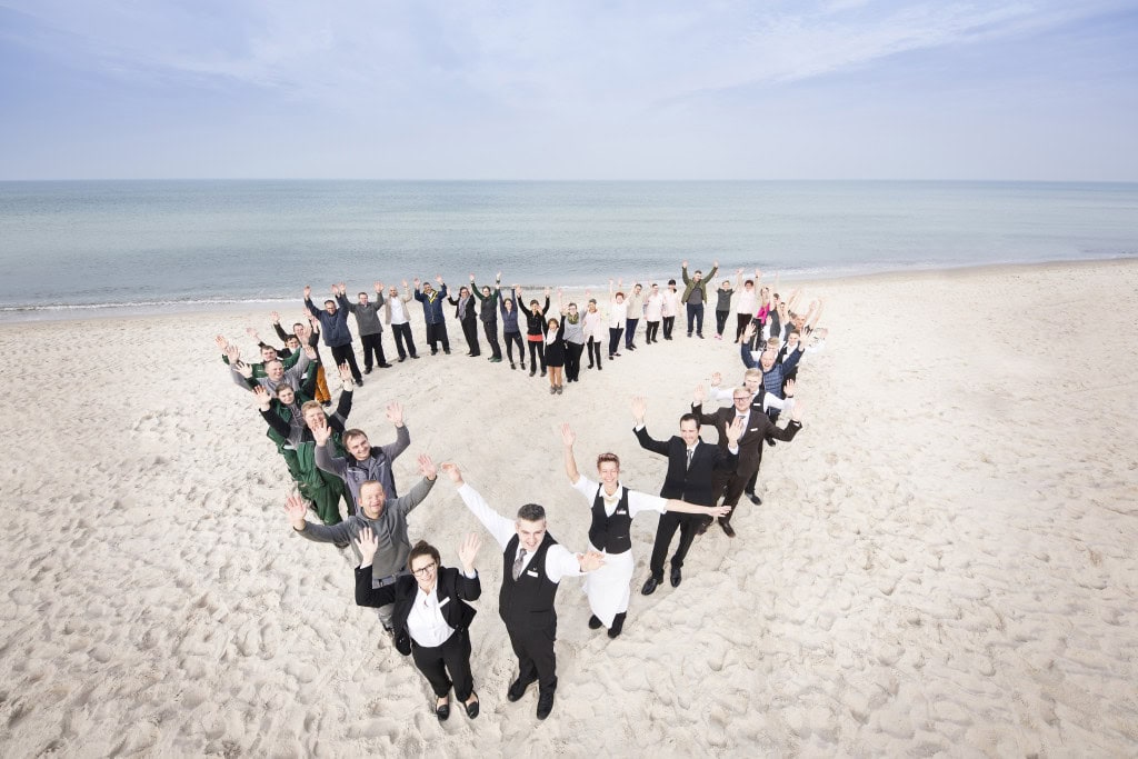 Mitarbeiter des Strandhotelfischlands formen ein Herz am Strand