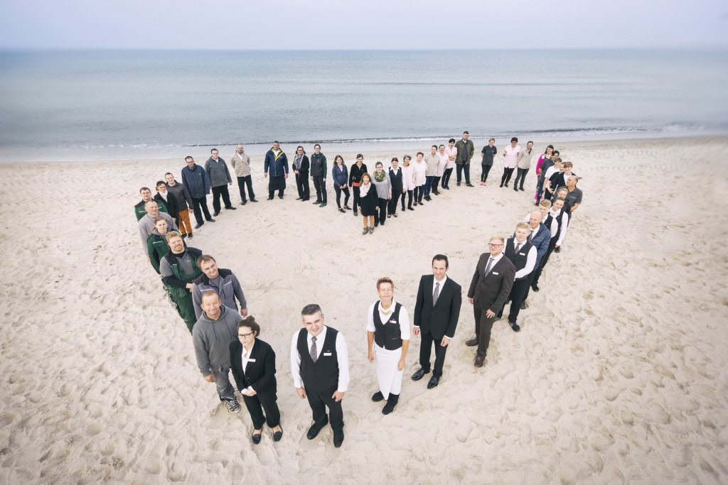 Mitarbeiter des Strandhotelfischlands formen ein Herz am Strand