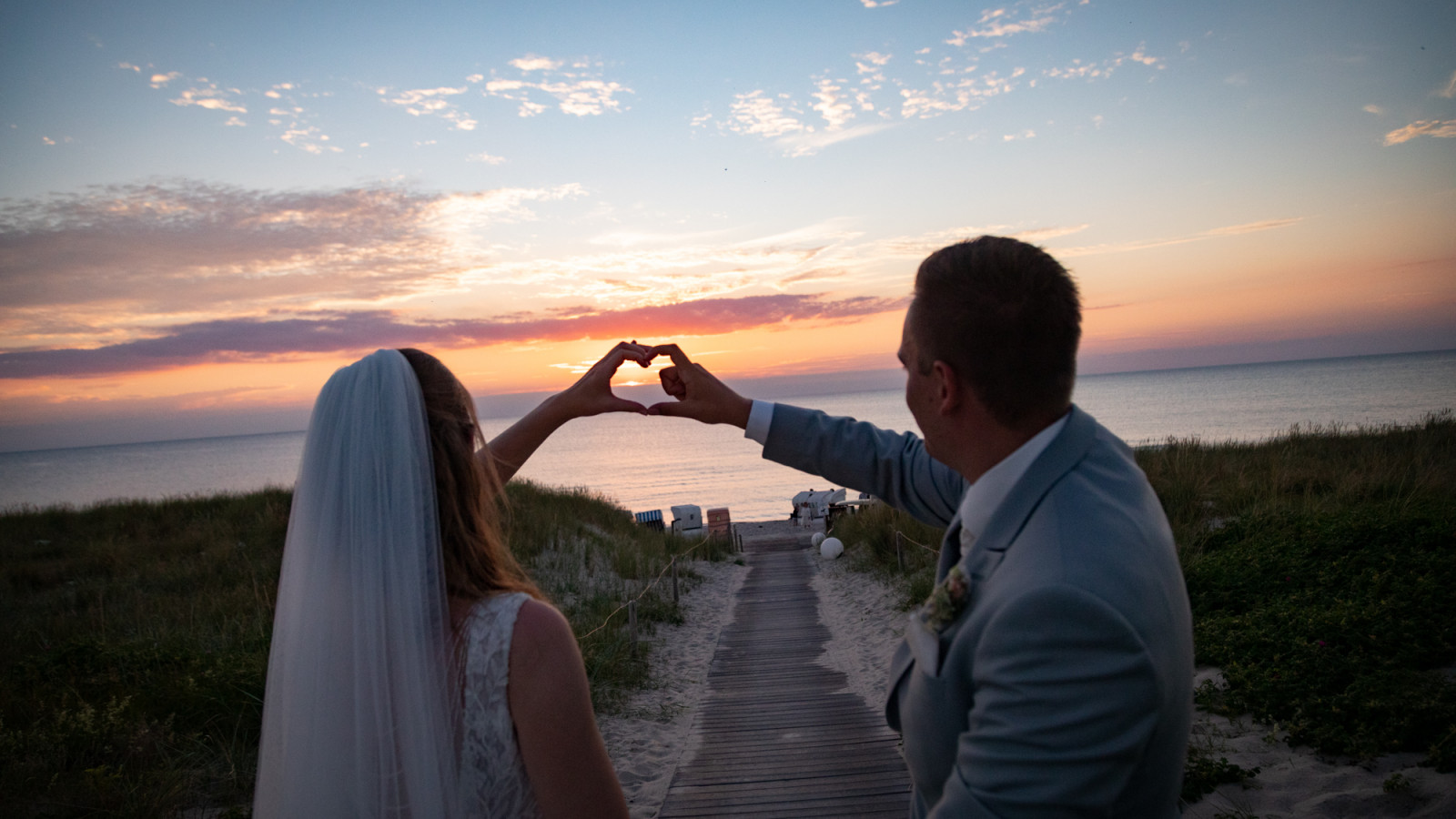 Braut und Bräutigam formen mit Händen ein Herz im Strandhotel Fischland