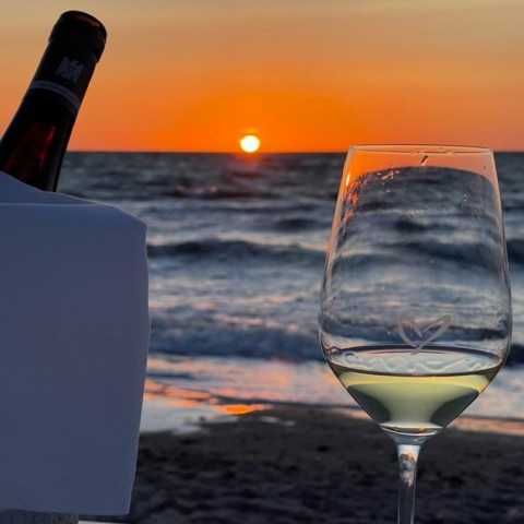 Weinglas mit Herz am Strand bei Sonnenuntergangsstimmung