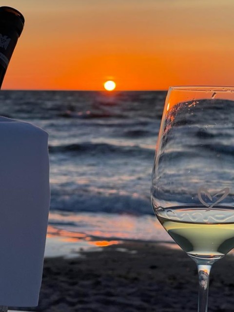 Weinglas mit Herz am Strand bei Sonnenuntergangsstimmung