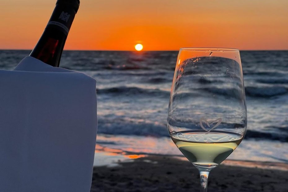 Weinglas mit Herz am Strand bei Sonnenuntergangsstimmung