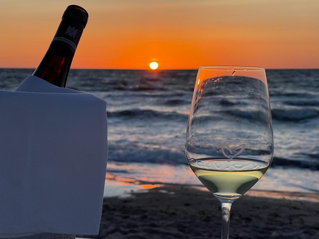 Weinglas mit Herz am Strand bei Sonnenuntergangsstimmung