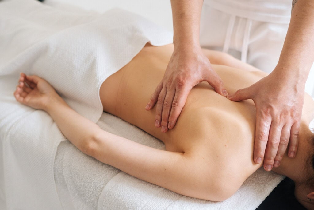 Male masseur massaging back and shoulder blades of young woman lying on massage table on white background. Concept of massage spa treatments.