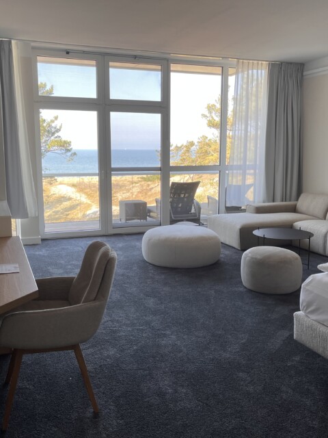 Suite im Strandhotel Fischland, Hauptraum mit Doppelbett, Couch, TV und Blick auf die Ostsee bei Sonnenschein