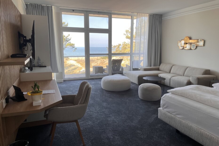 Suite im Strandhotel Fischland, Hauptraum mit Doppelbett, Couch, TV und Blick auf die Ostsee bei Sonnenschein